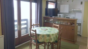 Cocina compacta con área de comedor, que incluye una mesa con sillas, un televisor y electrodomésticos básicos.