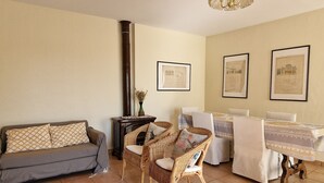 Ein gemütliches Wohnzimmer mit einer Couch, zwei Korbstühlen, einem Esstisch mit weißen Tischdecken und gerahmten Bildern an der Wand.