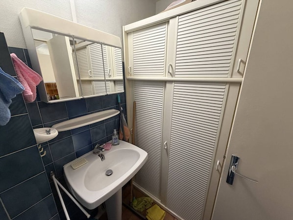 Une salle de bain avec un lavabo, un miroir et un dressing avec des portes à persiennes.