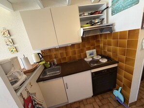 Une cuisine de taille réduite, équipée d’une cuisinière, d’un évier et de meubles blancs.