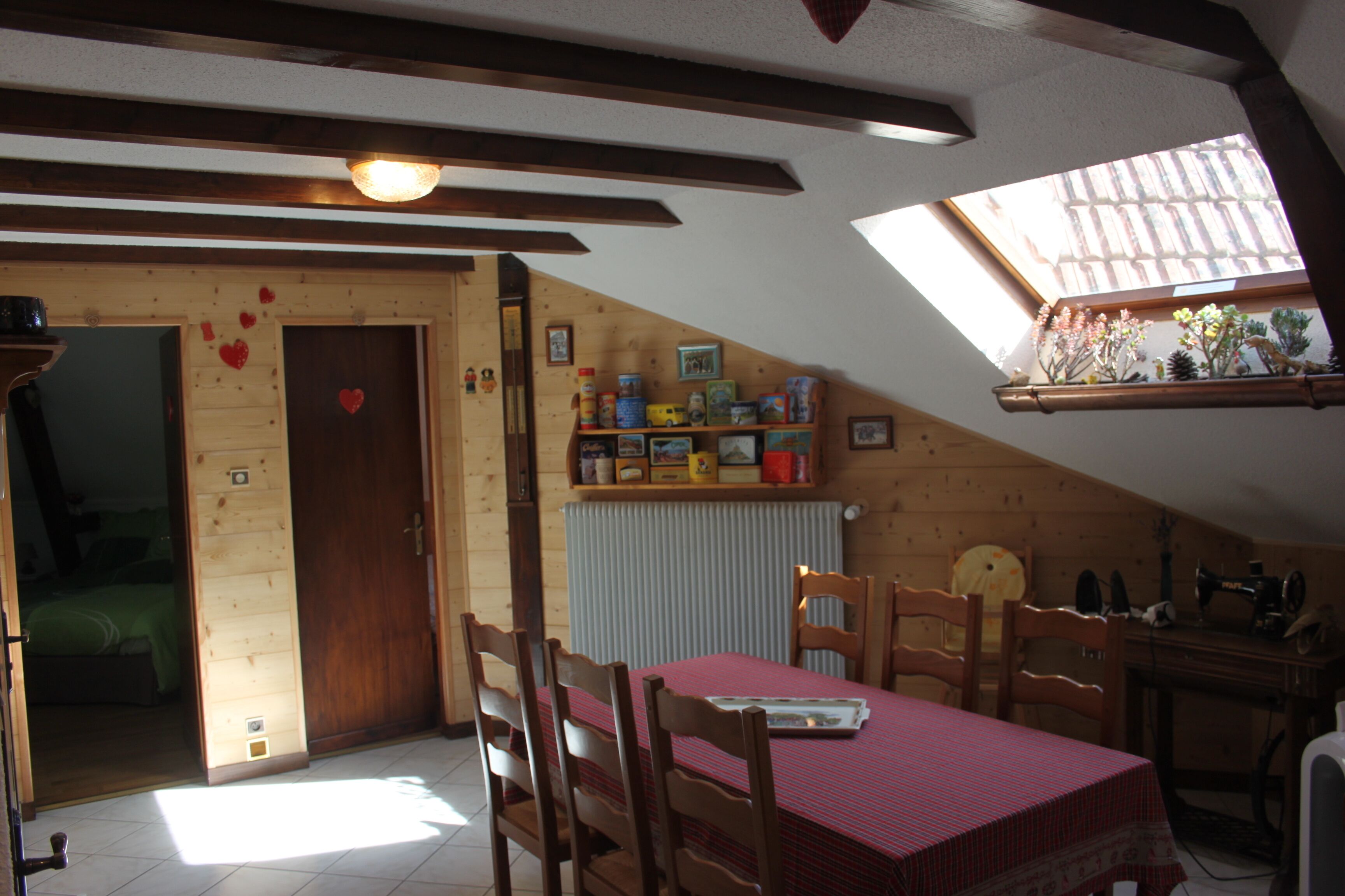 A cozy room with a wooden ceiling, a skylight, a dining table with chairs, and a radiator.