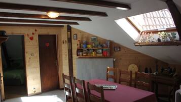 A cozy room with a wooden ceiling, a skylight, a dining table with chairs, and a radiator.