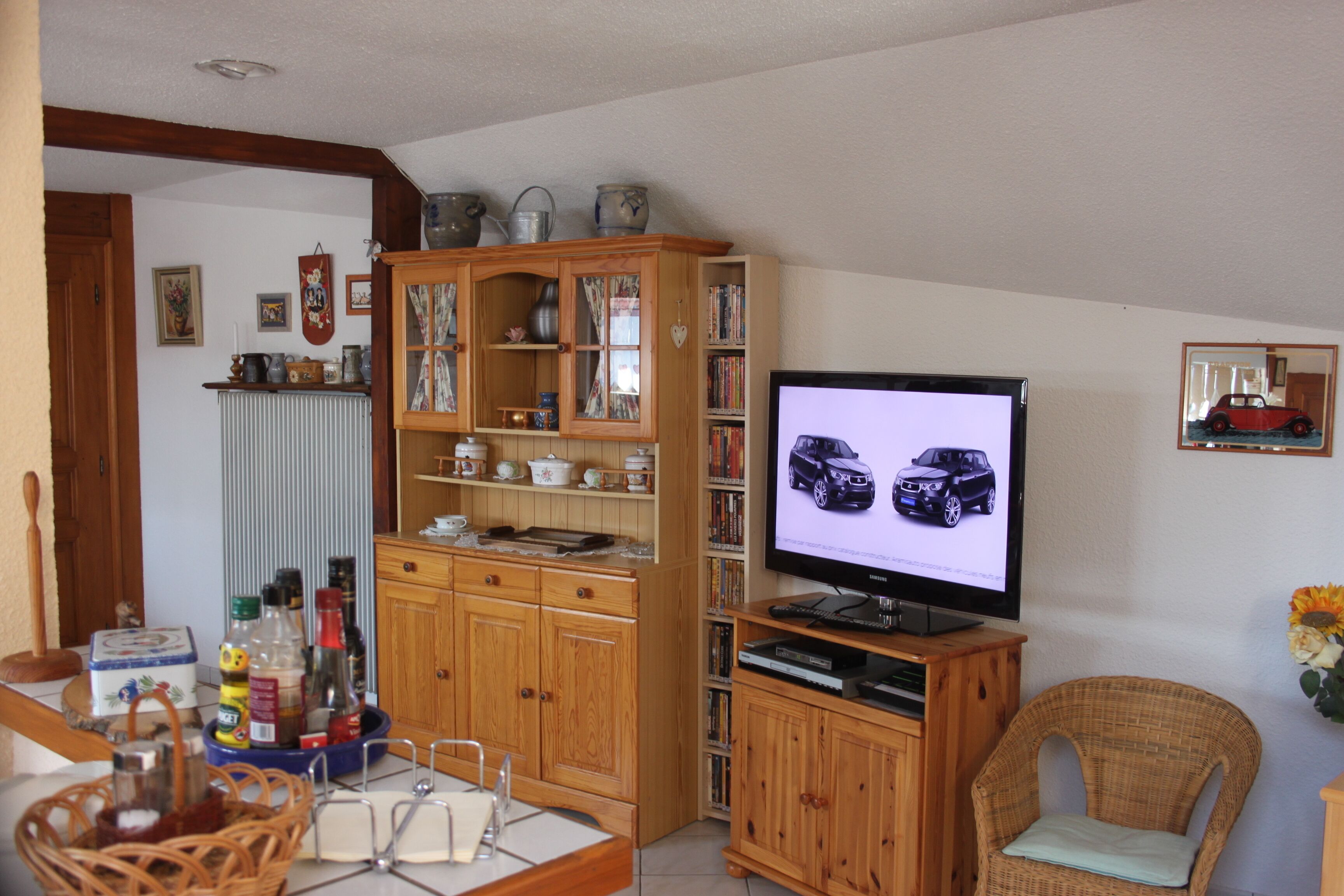 A living room with a television, wooden cabinets, a wicker chair, and a bookshelf.