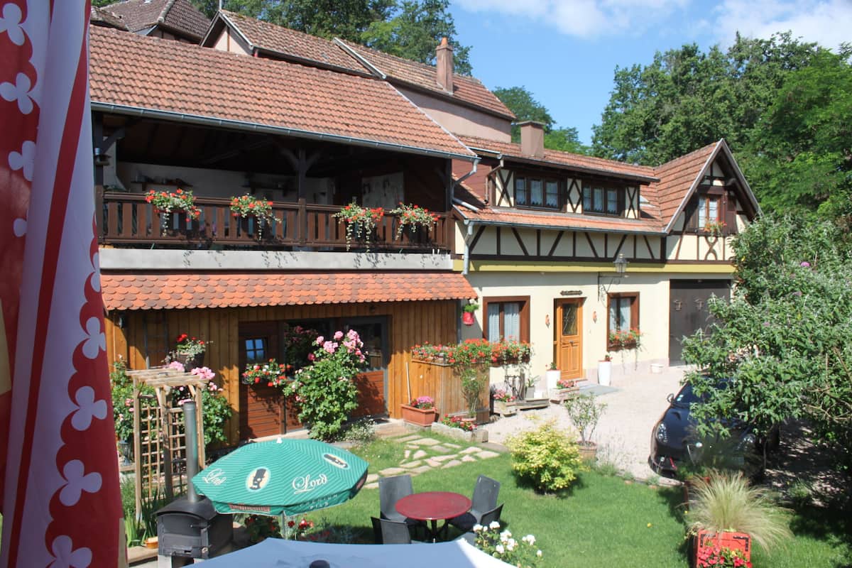 Un edificio de estilo europeo tradicional con un balcón de dos pisos, un jardín con mesa y sillas, y un coche estacionado en la entrada.