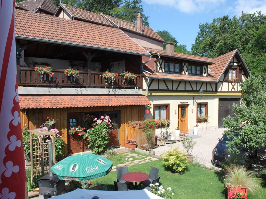 Un edificio de estilo europeo tradicional con un balcón de dos pisos, un jardín con mesa y sillas, y un coche estacionado en la entrada.