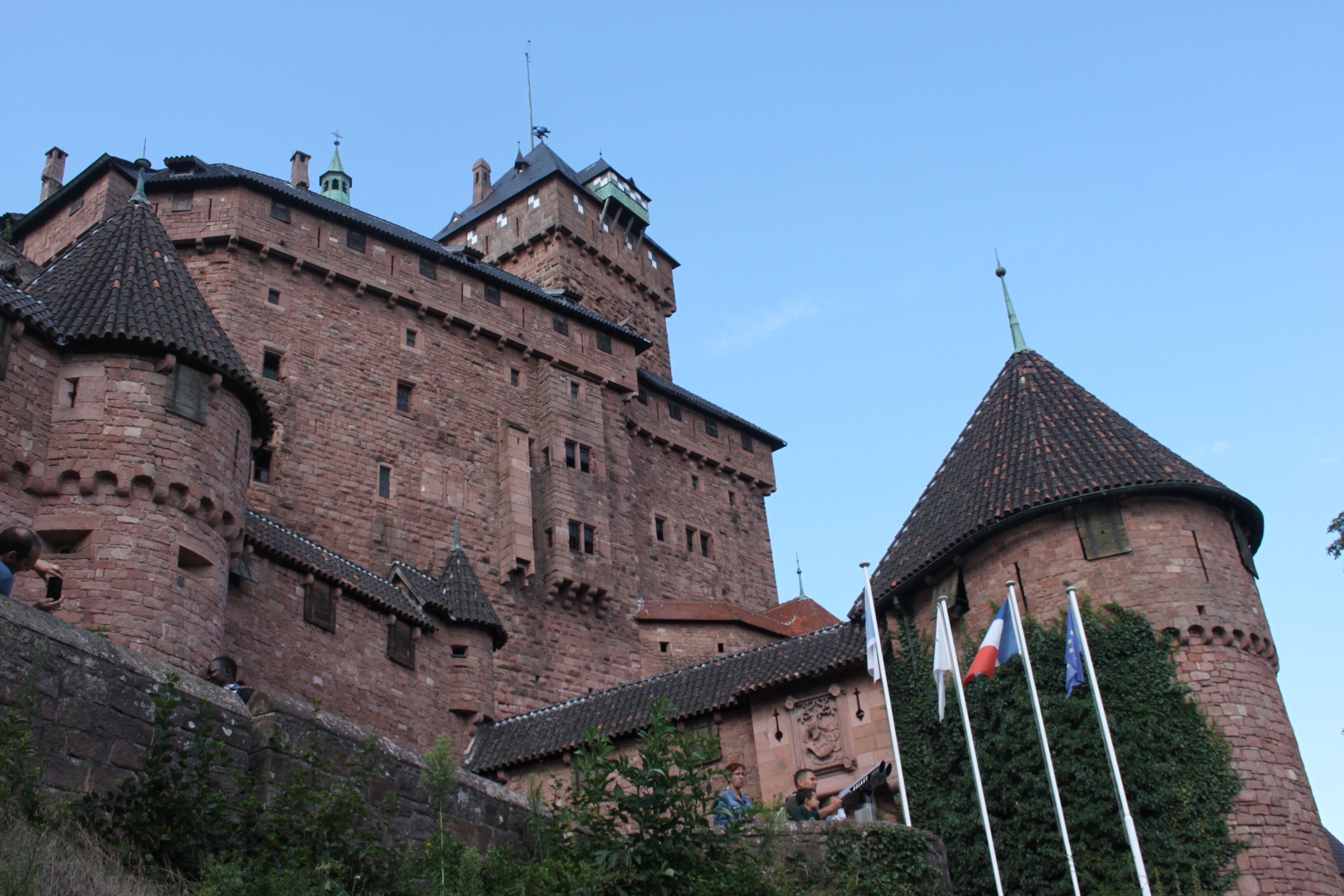Un château historique en briques, doté de nombreuses tours et arborant plusieurs drapeaux.