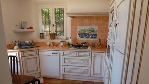 A kitchen with white cabinets, a tiled backsplash, and a dining area with a table and chairs. - Air-conditioned villa with heated pool, breathtaking sea view on the Levant Island (Cavalaire-Sur-Mer)