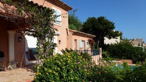 A house with a tiled roof, a garden with colorful flowers, and a swimming pool in the background. - Air-conditioned villa with heated pool, breathtaking sea view on the Levant Island (Cavalaire-Sur-Mer)