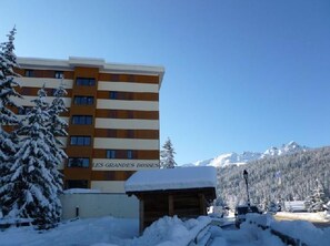 A hotel building with a sign reading "LES GRANDES BOSSES" in front of a snowy mountain backdrop.