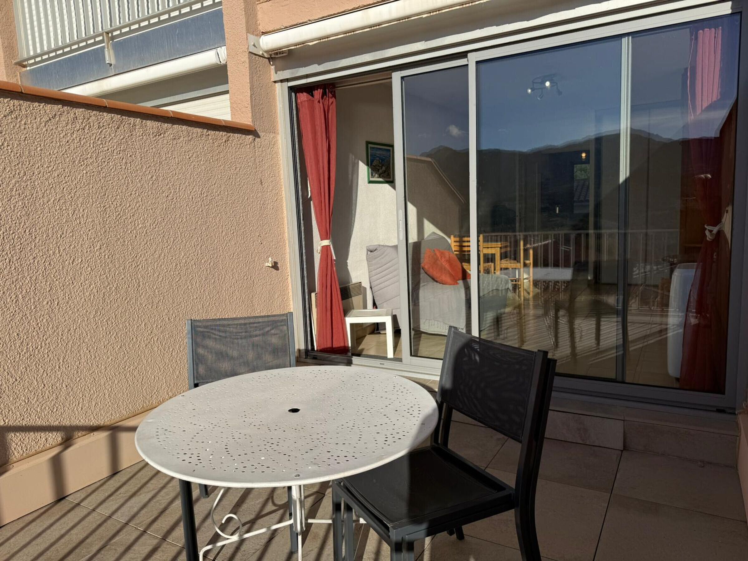 Patio esterno con tavolo rotondo e due sedie, porta scorrevole in vetro e vista sull'interno.