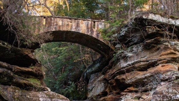 A waterfall cascading over rocks with a stone bridge in the background. - Sunrise Apt. - Peaceful Country Setting- Reasonable Distance to Hocking Hills  (Amanda)