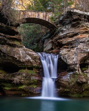 A waterfall cascading over rocks with a stone bridge in the background. - Sunrise Apt. - Peaceful Country Setting- Reasonable Distance to Hocking Hills  (Amanda)