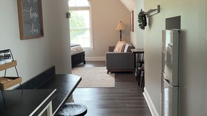 A modern kitchen with a dark countertop, a microwave, and a refrigerator. There is a dining area with a table and chairs, and a sofa in the background. - Sunrise Apt. - Peaceful Country Setting- Reasonable Distance to Hocking Hills  (Amanda)