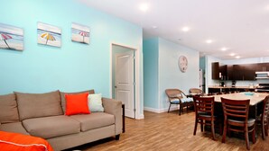 A living room with a sofa, chairs, and a dining table. There is a kitchen in the background with cabinets and a clock on the wall. - 8 Private Bedrooms+Bathrooms! HUGE POOL+KITCHEN+PRIVATE RETREAT By the Beach!!! (Myrtle Beach)