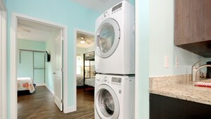 A laundry area with two stacked front-loading washing machines, a wooden floor, and a kitchen area with a granite countertop and a sink. - 8 Private Bedrooms+Bathrooms! HUGE POOL+KITCHEN+PRIVATE RETREAT By the Beach!!! (Myrtle Beach)