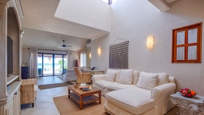 Een ruime woonkamer met een witte bank, een houten salontafel en een rieten fauteuil. Een groot raam biedt uitzicht op het strand.