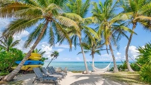 Een strand met palmbomen, een hangmat en ligstoelen.