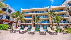 A multi-story hotel with a pool area, palm trees, and lounge chairs. - Luxury beachfront ground level condo, perfect for a family, pool access, WiFi (AKUMAL)