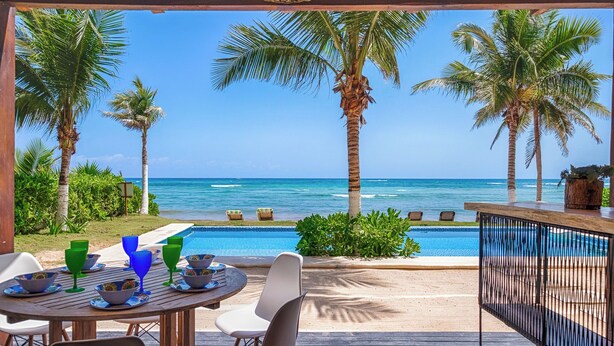 A poolside area with a view of the ocean, palm trees, and a bar. - Luxury beachfront ground level condo, perfect for a family, pool access, WiFi (AKUMAL)