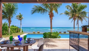 Zona de piscina con vistas al océano, palmeras y un bar.