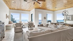Amplia sala de estar con techos altos, ventanas grandes con vistas al océano y un candelabro moderno.