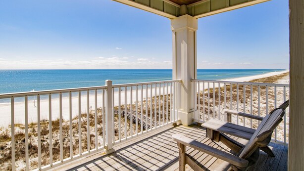 Una terraza de madera con barandilla blanca que da a una playa.