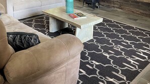 A rustic interior with a sofa, a coffee table, a fireplace, and a sign reading "FARM FRESH Eggs".
