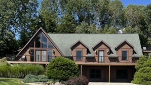 A two-story wooden cabin with a balcony and large windows, surrounded by a well-maintained lawn and trees.