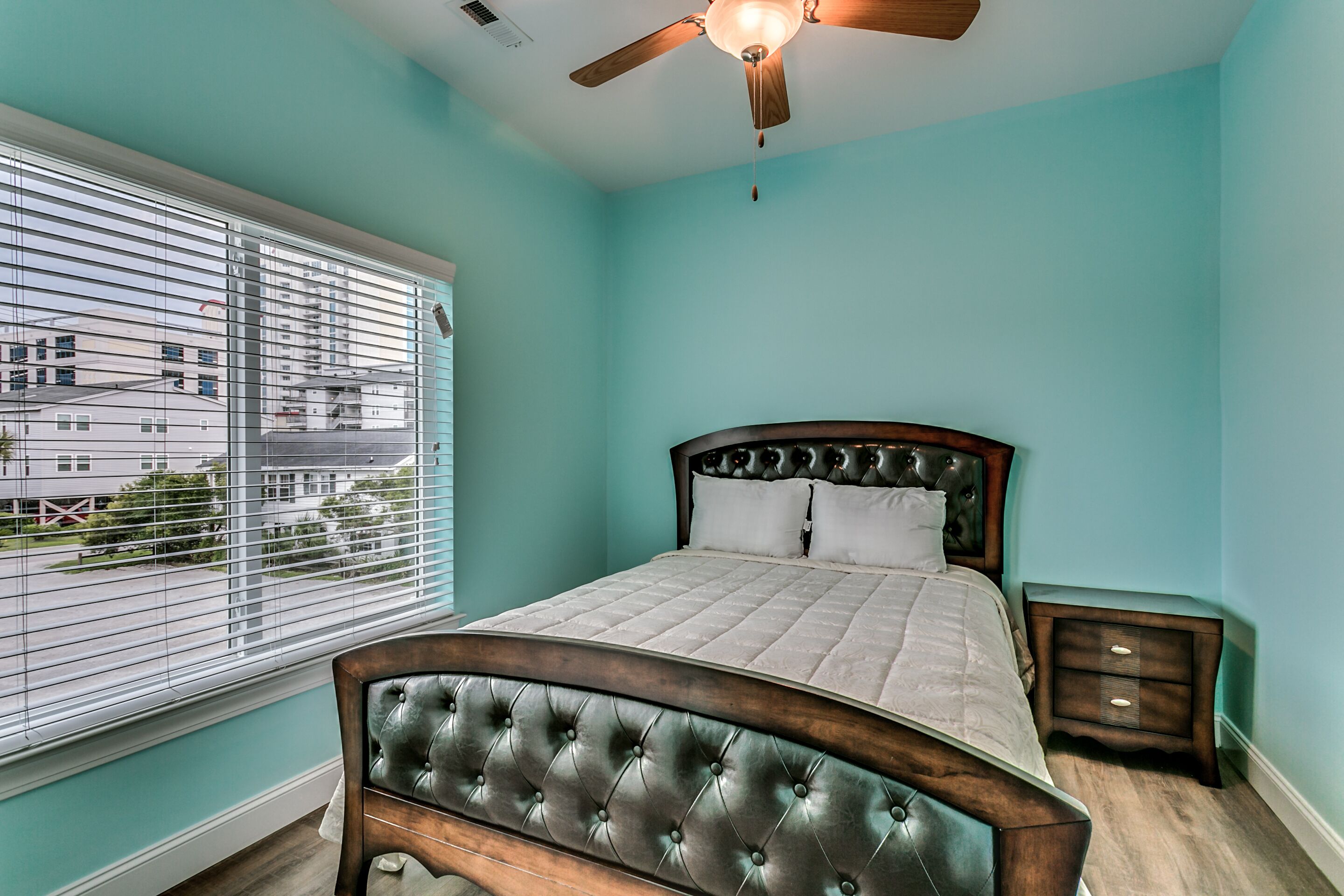 A bedroom with a bed, a ceiling fan, a window with blinds, and a nightstand.