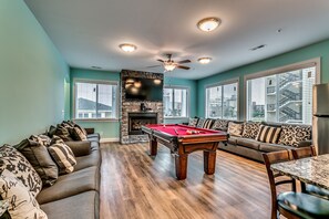 A living room with a pool table, a sofa, a dining table, and a fireplace.