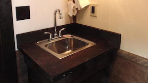 A bathroom with a dark wooden vanity, a stainless steel sink, a mirror with a deer silhouette, and a wall-mounted light fixture. - WATERFRONT and AFFORDABLE (Warrensburg)