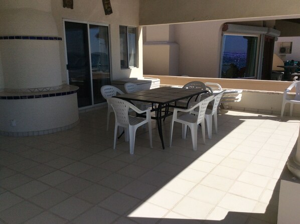 Een terras buiten met een tafel, stoelen, een barbecue en uitzicht op de stad.