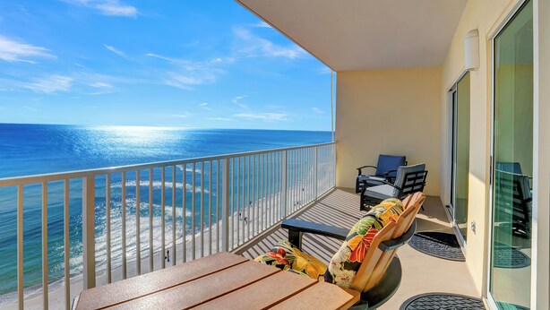 Un balcon avec vue sur l’océan, une table, des chaises et un canapé agrémenté de coussins colorés.