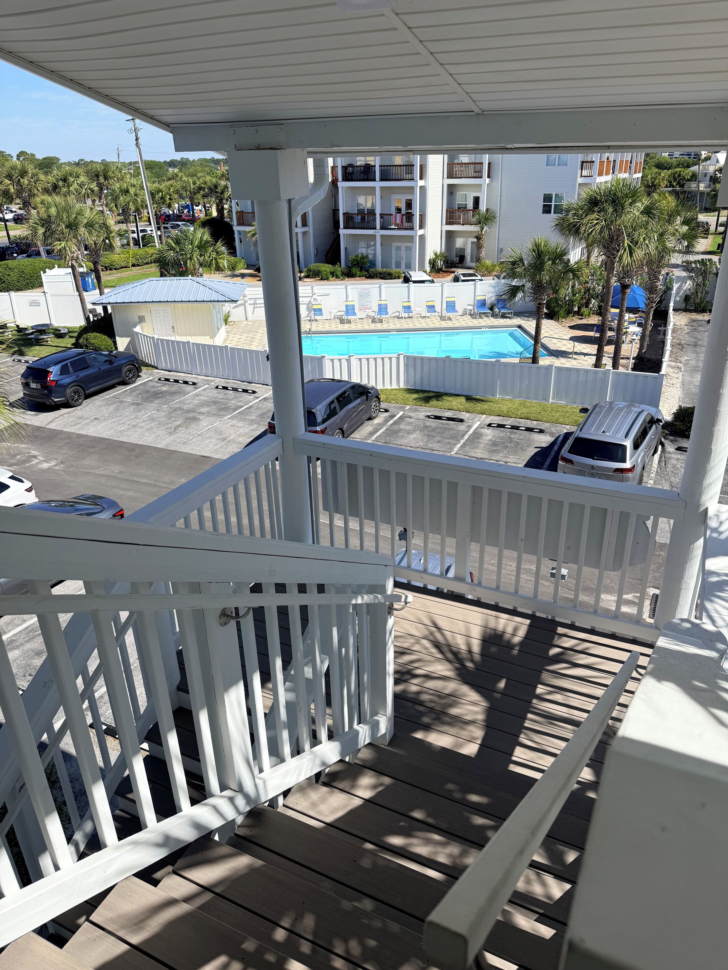 A balcony with a view of a swimming pool, a parking area, and a building with balconies.