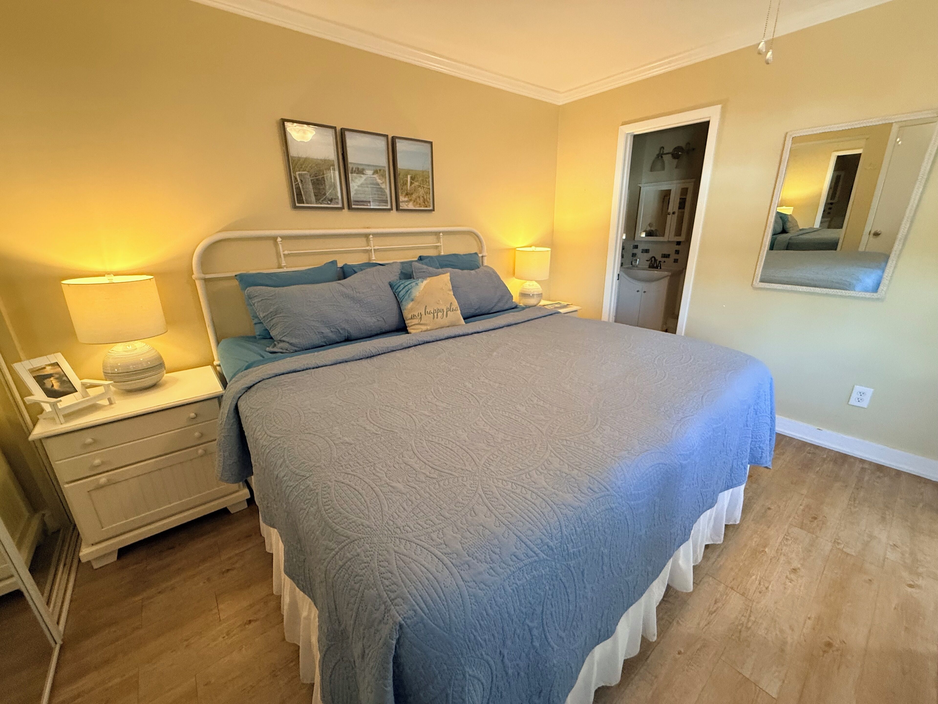 A bedroom with a bed, nightstands, a mirror, and a door leading to a bathroom.