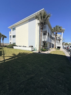 A multi-story building with balconies, a lawn, and palm trees.
