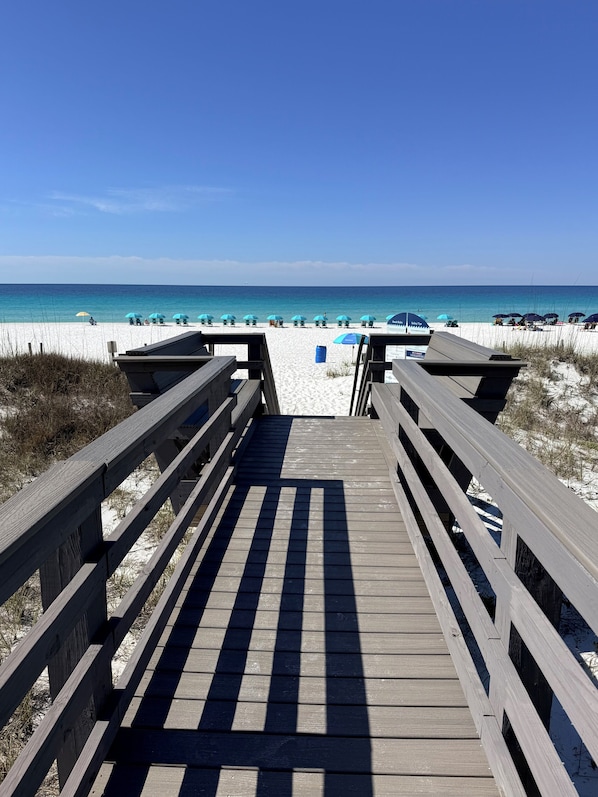 A wooden boardwalk leading to a beach with umbrellas and beach chairs.