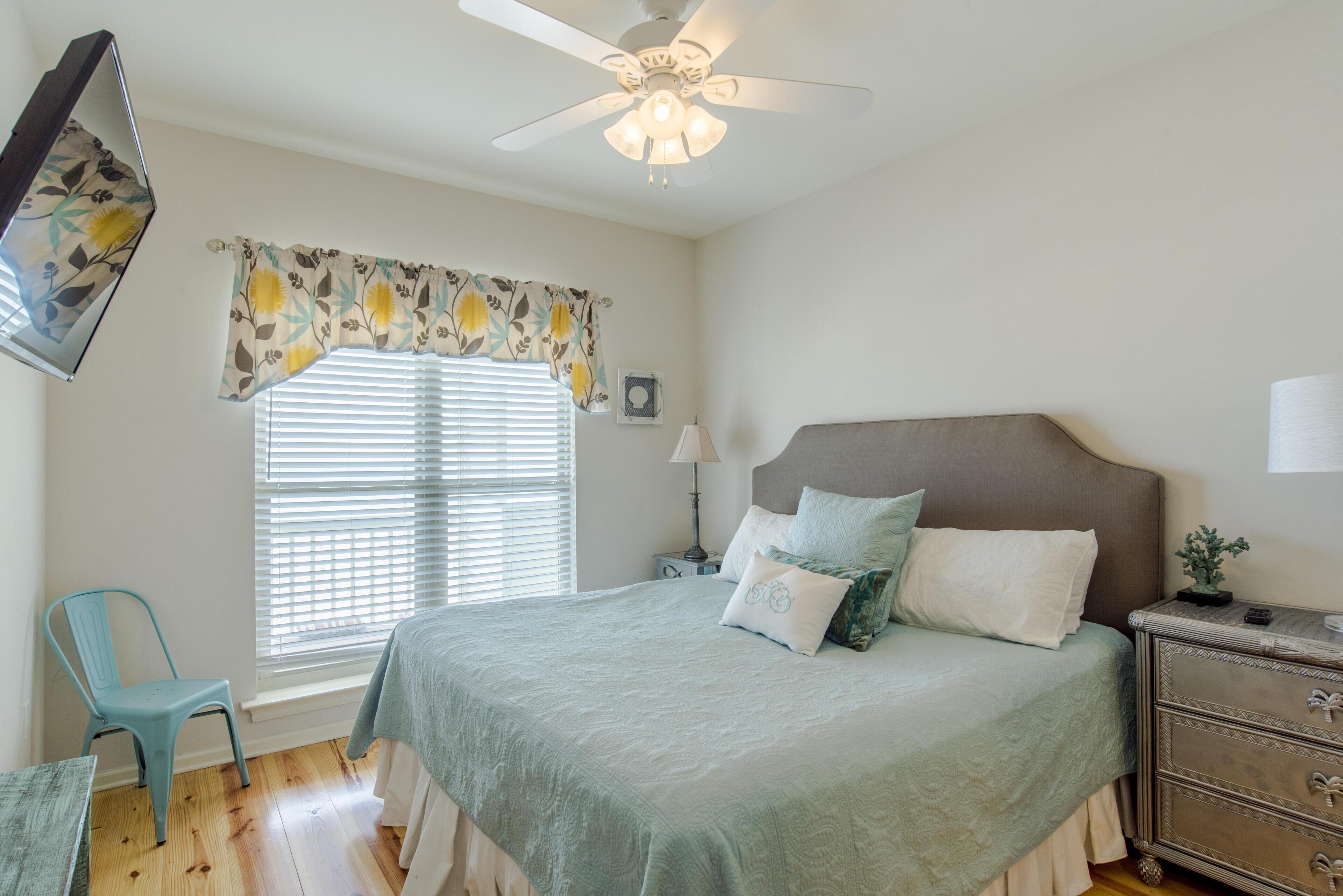 A bedroom with a bed, a nightstand, a chair, a ceiling fan, and a window with blinds.