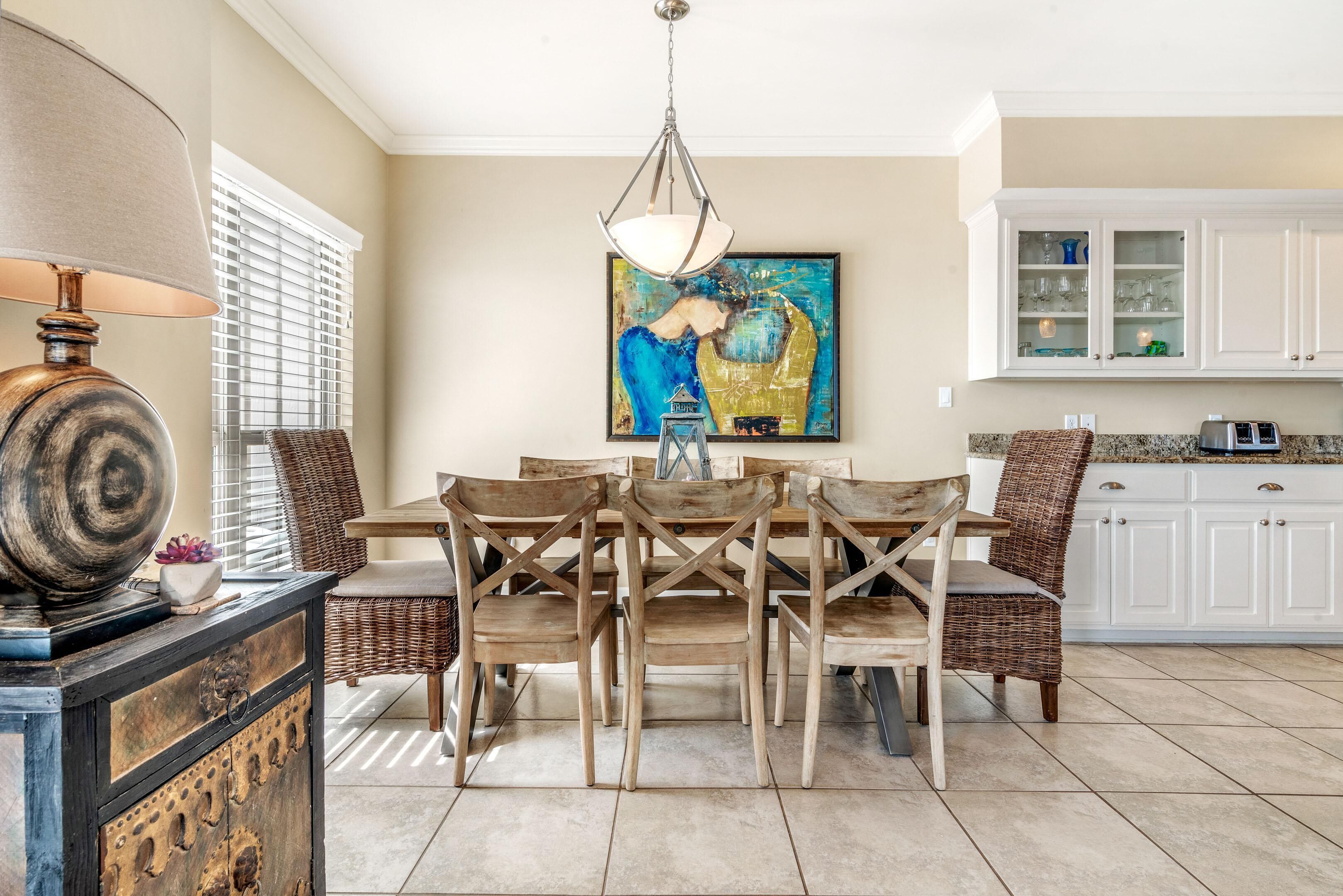 Un coin repas avec une table et des chaises, un tableau accroché au mur et une cuisine en arrière-plan.