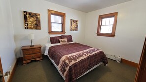 A bedroom with a bed, a nightstand, a lamp, and two windows with blinds. - Kaiser House Sleeps 8, Traverse City 3 minutes away!  Pet friendly   (Traverse City)