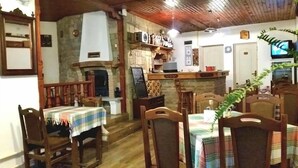 A cozy dining area with wooden chairs and tables, a stone fireplace, and a kitchen area with a TV and various appliances.