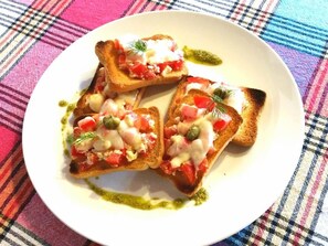 A plate with three pieces of toast topped with a creamy mixture, tomatoes, and capers, accompanied by a green sauce. - Family hotel Slavianska dusha (Veliko Tarnovo)