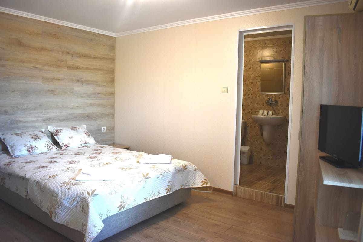 A bedroom with a bed, a television, and a bathroom visible through an open door.