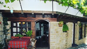 A rustic building with a stone facade, a wooden door, and a table with a plaid tablecloth.