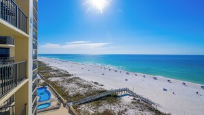 A beach view from a hotel balcony with a pool and a clear sky.
