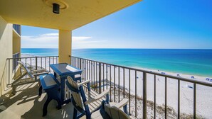 A balcony with a view of the beach, a table, chairs, and a railing.