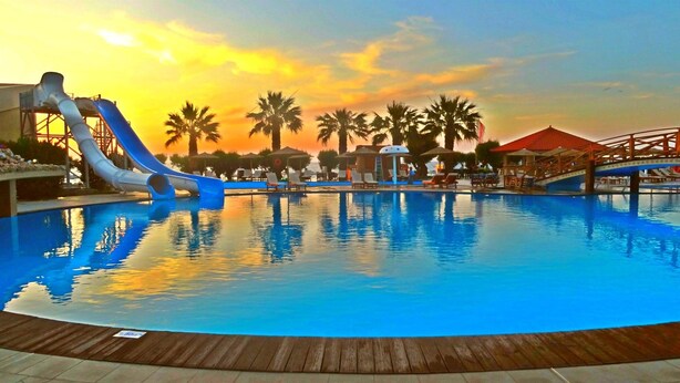 A swimming pool with a water slide, lounge chairs, and palm trees. - Club Marmara Doreta Beach Resort & Spa All Inclusive (Rhodes)