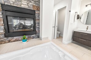 A bathroom with a stone wall, a bathtub, a sink with a mirror, and a toilet. - Private Retreat:master suite w Jacuzzi tub,game room,pool,outdoor entertainment! (North Myrtle Beach)