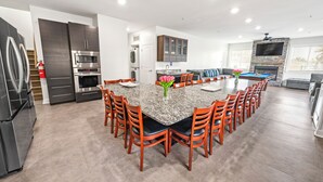 A modern kitchen with dark cabinets, a central island with chairs, and a built-in TV above the fireplace. - Private Retreat:master suite w Jacuzzi tub,game room,pool,outdoor entertainment! (North Myrtle Beach)