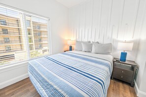 A hotel room with a large bed, a nightstand, a lamp, and a view of a building through the window. - Private Retreat:master suite w Jacuzzi tub,game room,pool,outdoor entertainment! (North Myrtle Beach)